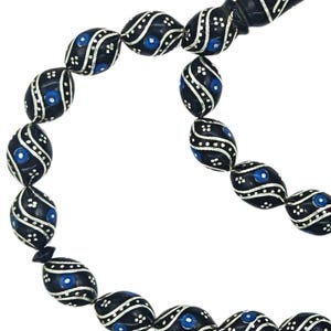 Può includere: Una corona di grani da preghiera con perline nere di forma ovale. Ogni perla è decorata con intricate linee ondulate color argento e piccoli punti bianchi, accentuati da un inserto circolare blu brillante su ogni lato della perla.