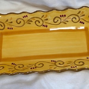 May include: Rectangular yellow serving platter with a scalloped edge. The platter features a hand-painted design of brown vines, swirls, and small red berries. The center is a lighter shade of yellow.