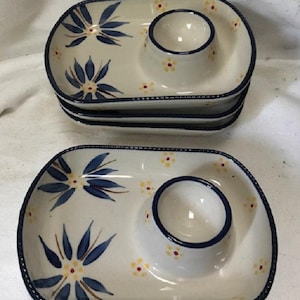 May include: Set of ceramic egg serving dishes. Each dish is oval-shaped with a built-in egg cup and decorated with blue floral designs and yellow flower accents. The edges are trimmed with a dark blue border.