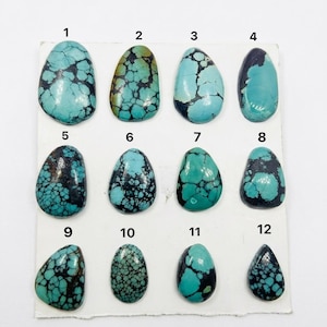 Puede incluir: Doce cabujones de turquesa pulidos dispuestos en una cuadrícula sobre una tarjeta blanca, numerados del 1 al 12. Cada piedra muestra tonos azules y verdes únicos con patrones de matriz marrón oscuro o negro, variando en forma y tamaño.
