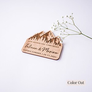 May include: A wooden wedding favor with a mountain range design and the text "Our Adventure Continues Tatiana & Maxime Quebec, Canada | 20.11.2021". The favor is in the color oat.