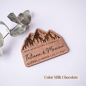 May include: Wooden wedding favor with a mountain range design. The text reads "Our adventure continues Tatiana & Maxime Quebec, Canada | 20.11.2021".