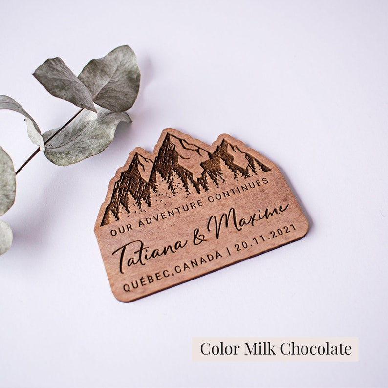 May include: Wooden wedding favor with a mountain range design. The text reads "Our adventure continues Tatiana & Maxime Quebec, Canada | 20.11.2021".