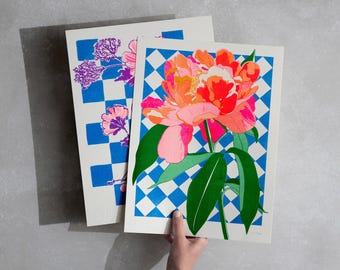 May include: Two prints with a blue and white checkered background. One print features a pink and orange peony flower with green leaves. The other print features a cluster of purple flowers.