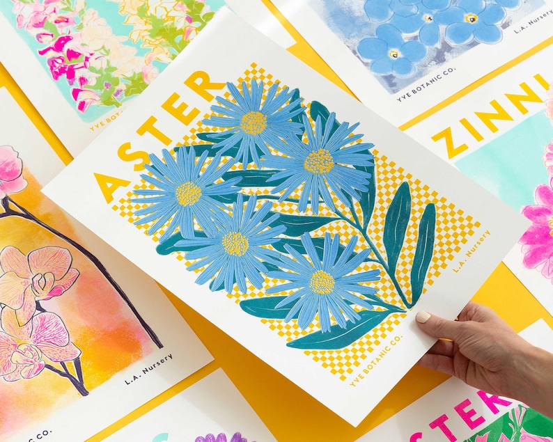 May include: A botanical art print showcasing blue aster flowers with yellow centres and green leaves, set against a yellow and white chequered background. The print is labelled "ASTER" and includes the text "YVE BOTANIC CO." and "L.A. Nursery".