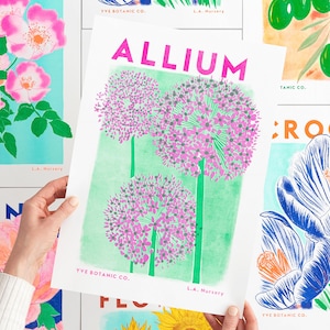 May include: A botanical illustration print featuring a purple Allium flower with green stems and leaves on a light green background. The print has the text "ALLIUM" in pink letters and "YVE BOTANIC CO." and "L.A. Nursery" in black letters.