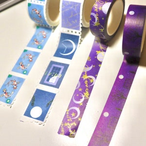 May include: Four rolls of decorative washi tape with different designs. The first roll has a blue background with white and gold koi fish. The second roll has a blue background with white and gold crescent moons and a window with a gold star. The third roll has a purple background with gold stars and crescent moons and the text "Moon over June." The fourth roll has a purple background with gold stars and a silhouette of a tree.
