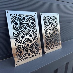 Può includere: Due pannelli da parete in metallo argentato con un design decorativo a taglio di forme a ventaglio sovrapposte.