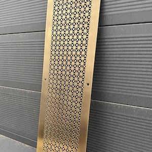 Puede incluir: Un panel decorativo de latón con un patrón geométrico de pequeñas estrellas. El panel es rectangular y tiene un borde ligeramente redondeado. Está hecho de metal y tiene un acabado cepillado.