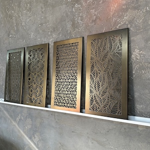 Könnte beinhalten: Vier dekorative Wandpaneele aus Metall mit verschiedenen geometrischen und floralen Mustern. Die Paneele sind goldfarben und haben eine Used-Look-Oberfläche.