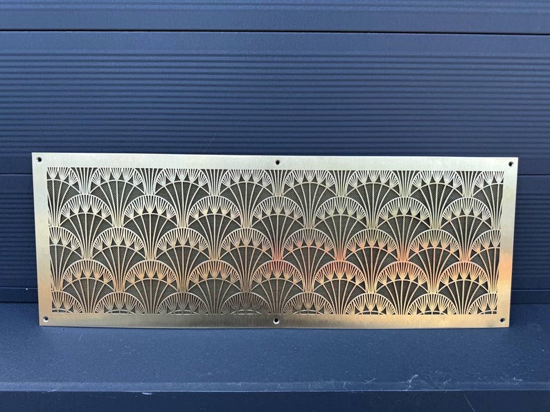 May include: A rectangular, gold-colored metal decorative panel with an Art Deco fan pattern. The panel has a series of repeating fan-shaped designs, with small holes at each corner and along the bottom edge.