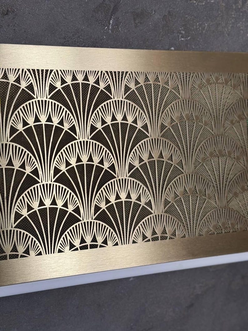 May include: A rectangular, Art Deco-style brass vent cover with a repeating fan-shaped pattern. The intricate design features a mesh backing, creating a contrast between the solid brass frame and the openwork design. The vent cover is a decorative element.