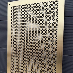 May include: A gold metal sheet with a geometric pattern of small holes. The sheet is mounted on a black wall.