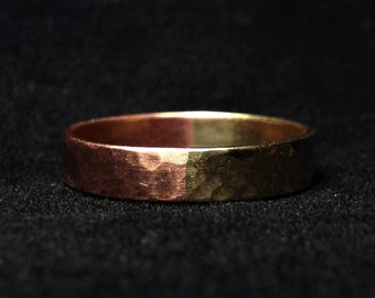 Puede incluir: Un anillo de metal martillado de dos tonos, con tonos cobrizos y dorados. El anillo tiene una superficie texturizada y un diseño sencillo. El anillo está sobre un fondo oscuro. El diámetro del anillo es de aproximadamente 2 cm.