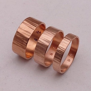 May include: Three copper rings with a hammered texture. The rings are stacked on top of each other. The rings are all the same size and have a shiny finish.