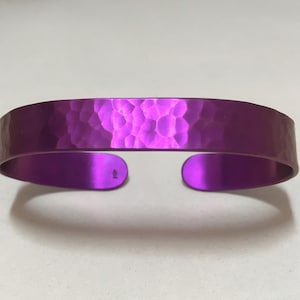 May include: A hammered purple metal bracelet. The bracelet is made of a smooth, shiny metal and has a slightly curved shape.