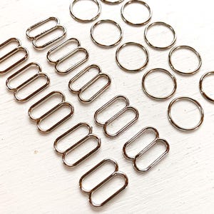 May include: A set of silver metal slider buckles and rings. The buckles are double-looped and come in various sizes. The rings are all the same size and are perfect for attaching to straps or other accessories.