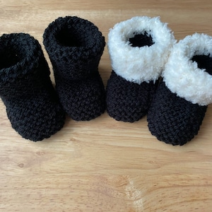 Puede incluir: Dos pares de botines de bebé tejidos. Un par es negro con un ribete blanco peludo. El otro par es completamente negro.