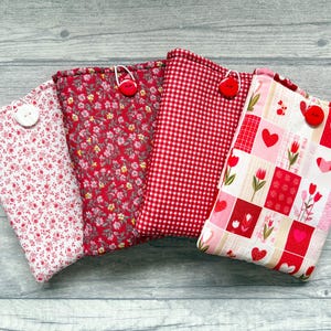 May include: Four rectangular fabric pouches featuring various red and white patterns. Each pouch is secured with a single button closure. The designs include small floral prints, a red and white gingham check, and a patchwork of hearts and tulips.