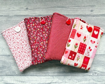 May include: Four rectangular fabric pouches featuring various red and white patterns. Each pouch is secured with a single button closure. The designs include small floral prints, a red and white gingham check, and a patchwork of hearts and tulips.