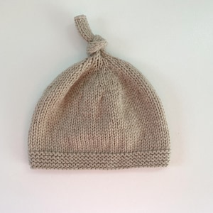 May include: A beige knitted baby hat with a knotted top.