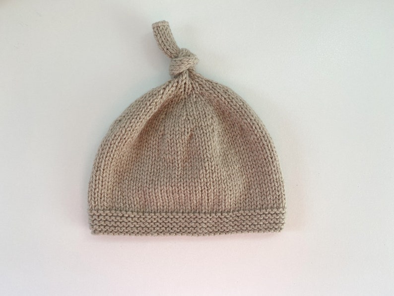 May include: A beige knitted baby hat with a knotted top.