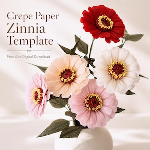 May include: A bouquet of five handcrafted crepe paper zinnia flowers in red, white, peach, and pink, featuring dark green leaves and stems. The text Crepe Paper Zinnia Template Printable Digital Download is visible on the left side of the image.