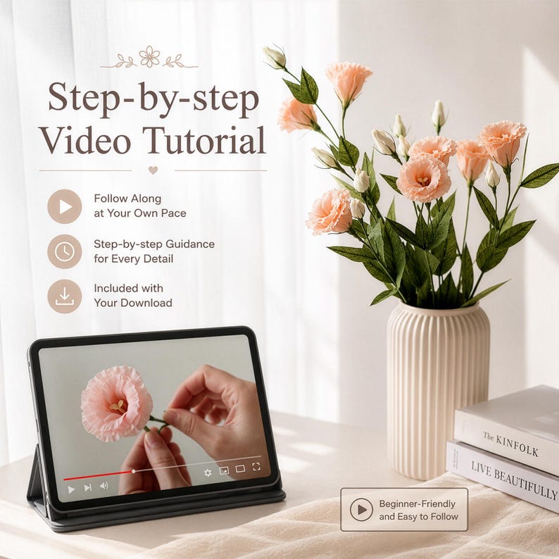 May include: A tablet displaying a step-by-step video tutorial on crafting a pink flower, positioned next to a ribbed cream vase containing a bouquet of artificial peach-coloured flowers and two stacked books titled The Kinfolk and Live Beautifully.