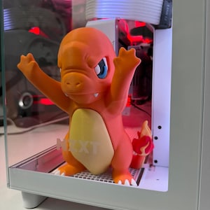 Peut inclure: Figurine Charmander imprimée en 3D, orange et crème, à l'intérieur d'un boîtier d'ordinateur. La figurine a les yeux bleus et les bras levés. Le boîtier de l'ordinateur porte le texte "NZXT".