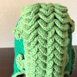 May include: Green crocheted hat with a unique textured design. The hat has a green and teal color scheme.