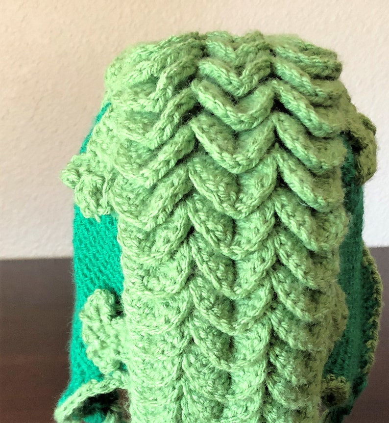 May include: Green crocheted hat with a unique textured design. The hat has a green and teal color scheme.