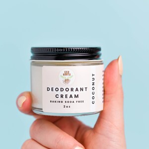 May include: A white jar with a black lid containing a coconut deodorant cream. The jar has a label that reads "Eco Roots Deodorant Cream Baking Soda Free 2 oz Coconut".