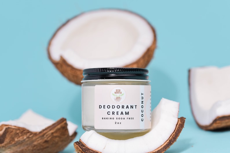 May include: A white jar of coconut deodorant cream with a black lid. The jar is sitting on top of a half coconut shell. The label on the jar reads "Eco Roots Deodorant Cream Coconut Baking Soda Free 2 oz."