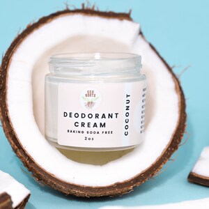May include: A white jar of coconut deodorant cream with a white label that says "Eco Roots Deodorant Cream Baking Soda Free 2 oz Coconut". The jar is sitting on a half of a coconut shell.