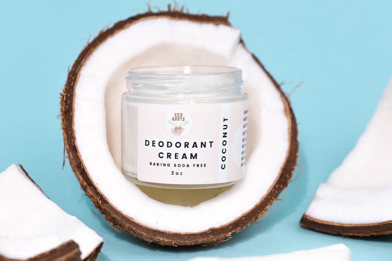 May include: A white jar of coconut deodorant cream with a white label that says "Eco Roots Deodorant Cream Baking Soda Free 2 oz Coconut". The jar is sitting on a half of a coconut shell.