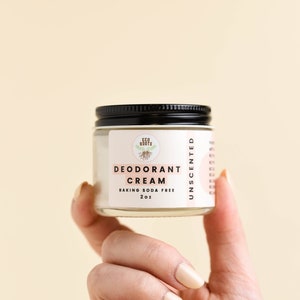 May include: A small glass jar with a black lid containing unscented deodorant cream. The label reads "Eco Roots Deodorant Cream Baking Soda Free 2 oz Unscented".