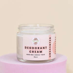 May include: A white jar of unscented deodorant cream with a pink label that reads "ECO ROOTS DEODORANT CREAM BAKING SODA FREE 2oz UNSCENTED".
