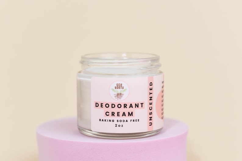 May include: A white jar of unscented deodorant cream with a pink label that reads "ECO ROOTS DEODORANT CREAM BAKING SODA FREE 2oz UNSCENTED".