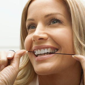 Puede incluir: Una mujer sonr&iacute;e mientras usa hilo dental en sus dientes con un hilo dental negro.