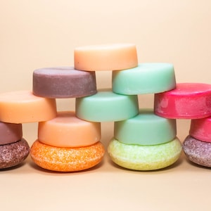 Pode incluir: Uma cole&ccedil;&atilde;o de barras de shampoo s&oacute;lidas coloridas empilhadas em forma de pir&acirc;mide. As barras s&atilde;o em tons de rosa, laranja, marrom e verde.