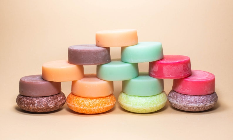 Pode incluir: Uma cole&ccedil;&atilde;o de barras de shampoo s&oacute;lidas coloridas empilhadas em forma de pir&acirc;mide. As barras s&atilde;o em tons de rosa, laranja, marrom e verde.