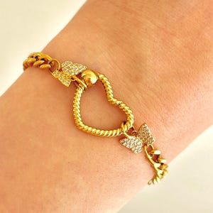 May include: Gold-toned bracelet featuring a heart-shaped centerpiece and butterfly accents. The bracelet has a curb chain design and is adorned with sparkling embellishments. The heart and butterflies are detailed with small, clear stones.