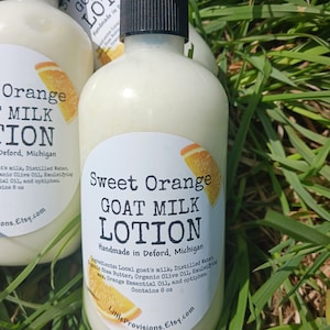 May include: A white bottle of Sweet Orange Goat Milk Lotion, handmade in Deford, Michigan. The bottle has a black pump top and a white label with orange text. The label lists the ingredients: local goat's milk, distilled water, shea butter, organic olive oil, emulsifying wax, orange essential oil, and optiphen. The bottle contains 8 ounces of lotion.