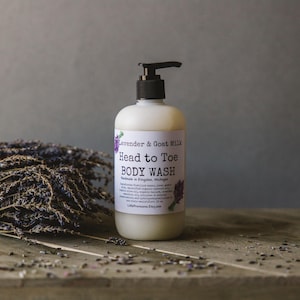 Op de afbeelding: Een witte plastic fles met een zwarte pompdispenser gevuld met een witte vloeistof. De fles heeft een etiket met de tekst "Lavender & Goat Milk Head to Toe BODY WASH Handmade in Kingston, Michigan LittleProvisions.Etsy.com".
