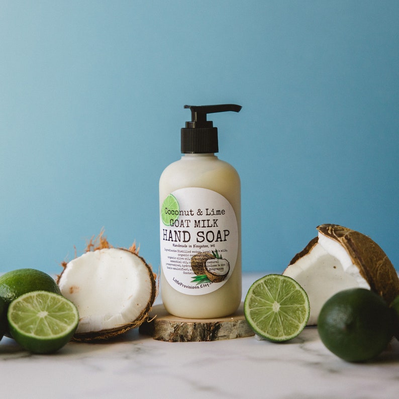 May include: A white bottle of Coconut & Lime Goat Milk Hand Soap, handmade in Kingston, MI. The bottle is sitting on a wooden slice with limes and coconuts around it.