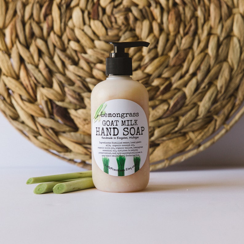 May include: A clear bottle of lemongrass goat milk hand soap with a black pump top. The bottle has a white label with black text that reads "Lemongrass Goat Milk Hand Soap Handmade in Kingston, Michigan". The label also includes a list of ingredients.