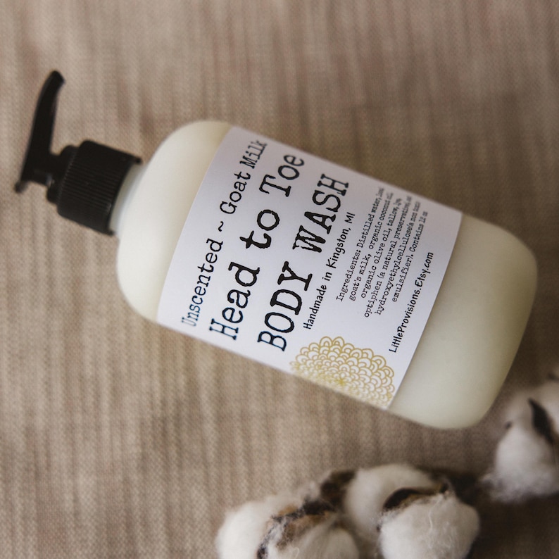 Op de afbeelding: Een witte plastic fles met een zwarte pomp. De fles is gelabeld met "Unscented Goat Milk Head to Toe BODY WASH" en "Handmade in Kingston, MI". Het etiket vermeldt ook de ingredi&euml;nten, waaronder geitenmelk, biologische olijfolie en andere natuurlijke ingredi&euml;nten.