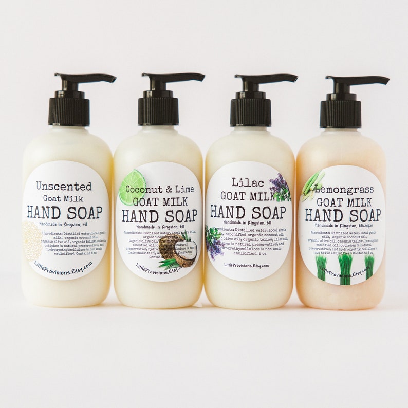 May include: Four clear plastic bottles of goat milk hand soap with pump tops. The bottles are labeled with different scents: Unscented, Coconut & Lime, Lilac, and Lemongrass. Each label includes the text "Goat Milk Hand Soap" and "Handmade in Kingston, MI".