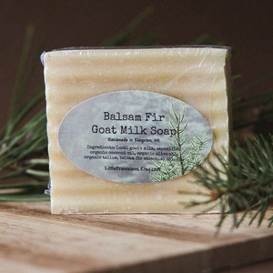 May include: A bar of Balsam Fir Goat Milk Soap, handmade in Kingston, MI. The soap is wrapped in clear plastic and has a white label with black text. The label reads "Balsam Fir Goat Milk Soap Handmade in Kingston, MI Ingredients: Local goat's milk, saponified organic coconut oil, organic olive oil, organic tallow, Balsam Fir essential oil Little Provisions. Etsy.com"