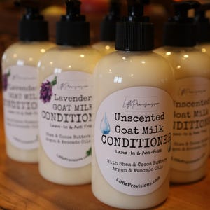 May include: Several bottles of goat milk conditioner with black pump tops are arranged on a wooden surface. The labels include text such as "Unscented Goat Milk Conditioner" and "Lavender Goat Milk Conditioner".